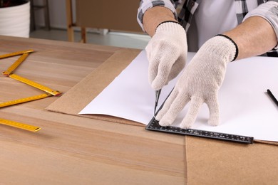 Worker cutting paper with utility knife and ruler at wooden table indoors, closeup