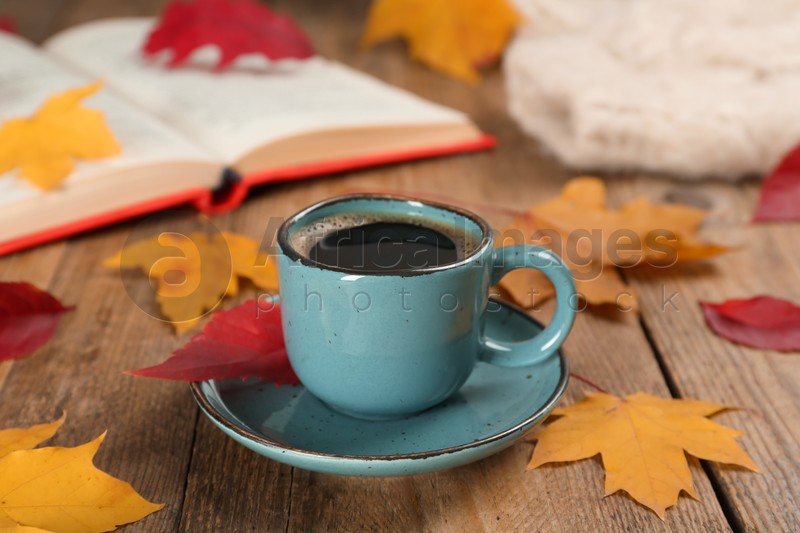 Cup of hot coffee and autumn leaves on wooden table