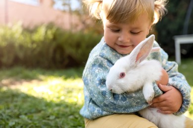 Photo of Happy little girl with cute rabbit on green grass outdoors, closeup. Space for text
