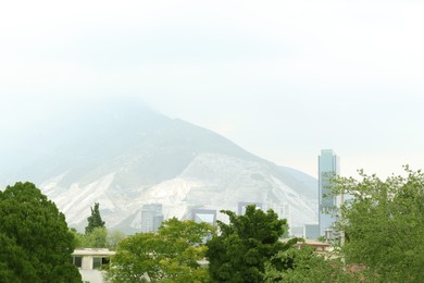 Photo of Picturesque view of city with buildings and trees near mountains