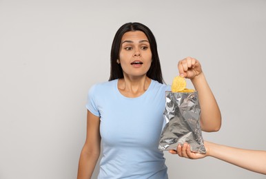 Beautiful young woman eating tasty potato chips on grey background