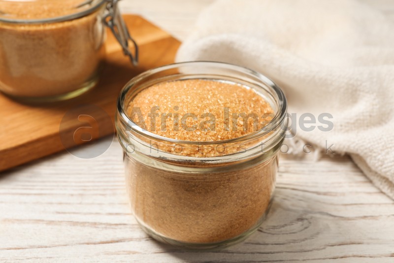 Photo of Glass jar with brown sugar on white wooden table, closeup