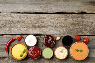 Many different sauces on wooden table, flat lay. Space for text