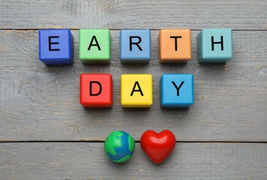 Photo of Colorful cubes with words Earth Day, plasticine planet and decorative heart on grey wooden table, flat lay