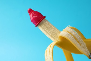 Banana with condom on light blue background, space for text. Safe sex concept