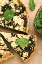 Photo of Delicious homemade quiche and fresh spinach leaves on parchment paper, flat lay