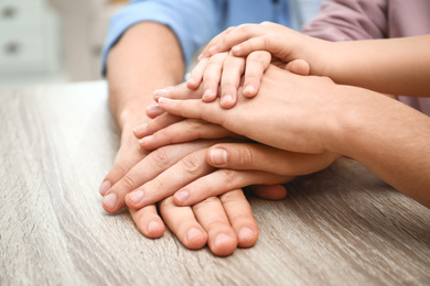 Happy family holding hands at wooden table indoors, closeup view