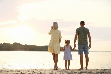 Happy parents with their child on beach, back view. Spending time in nature