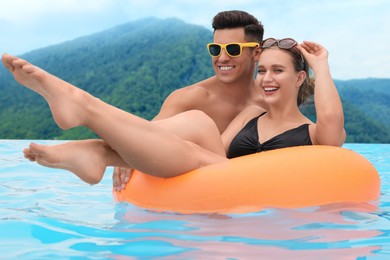 Happy couple in outdoor swimming pool at luxury resort with beautiful view of mountains