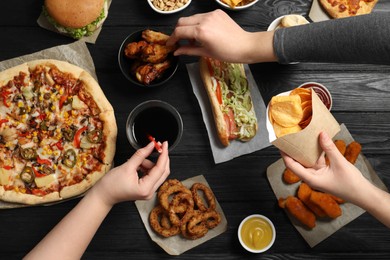 Photo of Friends eating pizza, chicken wings and other fast food at black wooden table, top view