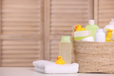 Photo of Wicker basket with baby cosmetic products, bath accessories and rubber ducks on table indoors. Space for text