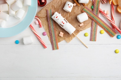 Flat lay composition with funny snowman made of marshmallows on white wooden table. Space for text