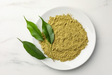 Photo of Henna powder and green leaves on white marble table, top view. Natural hair coloring