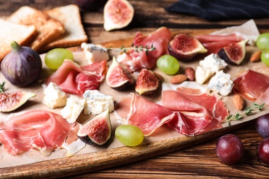 Ripe figs and prosciutto served on wooden table, closeup