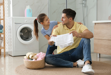 Father and little daughter with clean laundry in bathroom
