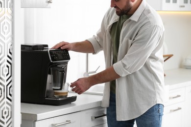 Young man preparing fresh aromatic coffee with modern machine in kitchen, closeup