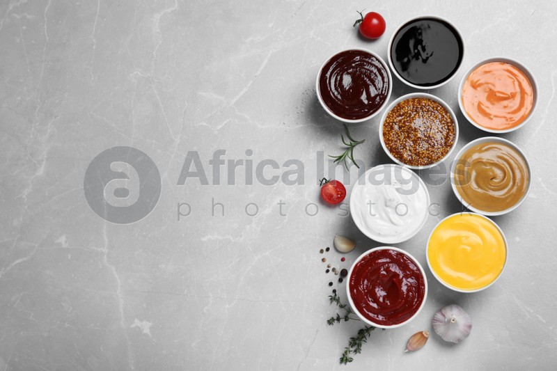 Many different sauces on light grey table, flat lay. Space for text