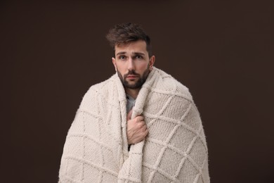 Man wrapped in blanket suffering from fever on brown background. Cold symptoms
