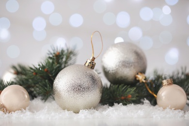 Beautiful Christmas balls and fir branches on snow against blurred festive lights