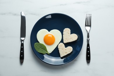 Romantic breakfast with heart shaped fried egg served on white marble table, flat lay
