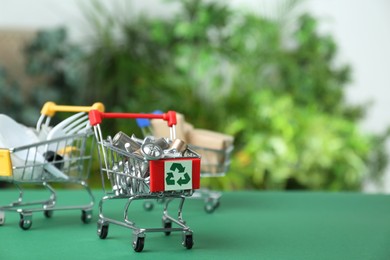 Photo of Shopping cart with recycling symbol full of garbage on green table, space for text