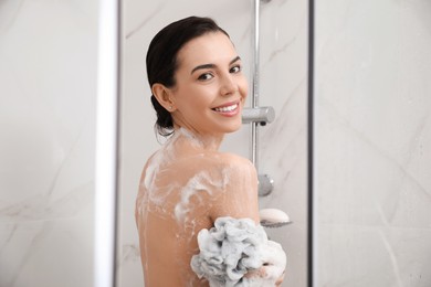 Photo of Young woman with mesh pouf taking shower at home