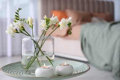 Vase with beautiful freesia flowers and burning candles on stand in bedroom, space for text. Interior elements