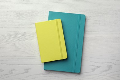 Yellow and turquoise planners on white wooden table, top view
