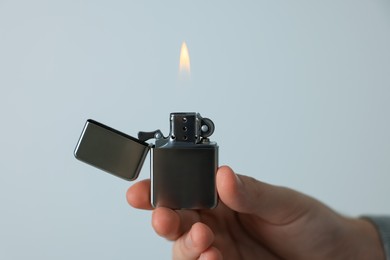 Man holding lighter with burning flame against light grey background, closeup