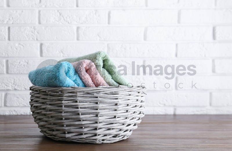 Wicker basket with soft bath towels on wooden table near white brick wall