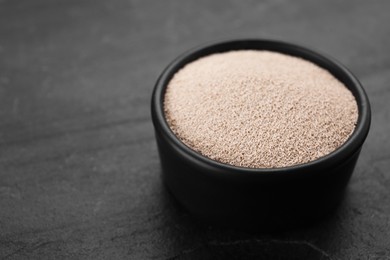 Photo of Bowl of active dry yeast on black table, closeup. Space for text