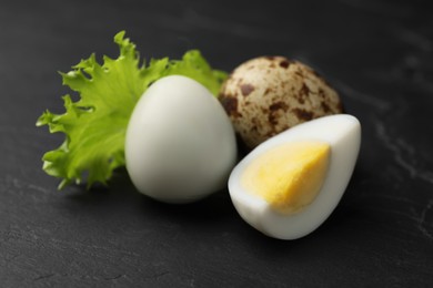 Photo of Unpeeled and peeled hard boiled quail eggs with lettuce leaf on black table, closeup