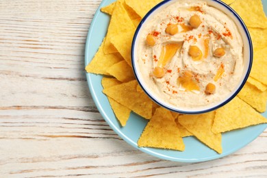 Bowl of tasty hummus with chickpeas, paprika and crispy chips on white wooden table, top view. Space for text