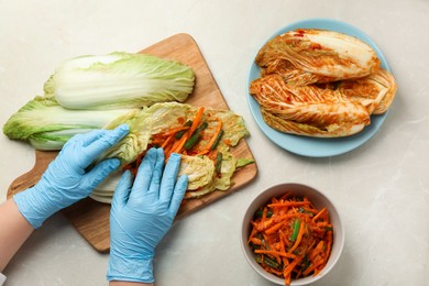 Photo of Woman preparing spicy cabbage kimchi at beige marble table, top view