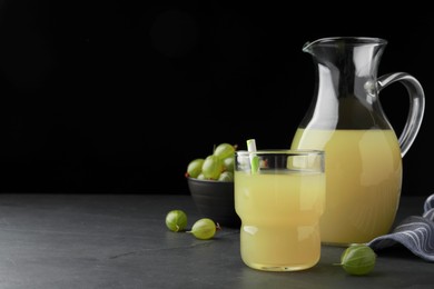Photo of Tasty gooseberry juice on black table against dark background. Space for text