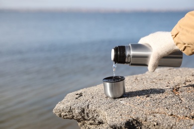Photo of Woman pouring hot drink into cup from thermos outdoors, closeup