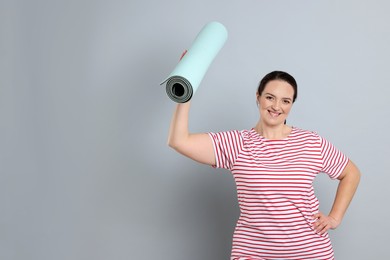 Happy overweight woman with yoga mat on grey background, space for text
