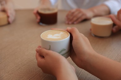 Woman holding cup of coffee spending time with friends in cafe, closeup