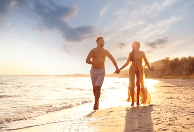 Happy young couple running together on beach at sunset