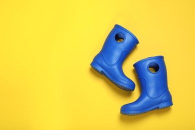 Pair of bright blue rubber boots on yellow background top view. Space for text