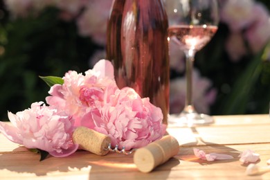 Photo of Rose wine and corkscrew near beautiful peonies on wooden table in garden, closeup