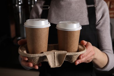 Barista holding takeaway paper cups with coffee in cafe, closeup