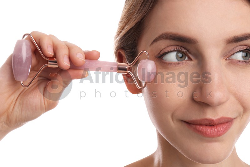 Photo of Young woman using natural rose quartz face roller on white background, closeup