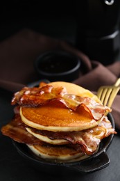 Delicious pancakes with maple syrup and fried bacon on black table
