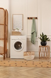 Photo of Laundry room interior with modern washing machine and beautiful houseplant near white wall