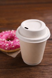 Photo of Tasty frosted donut with sprinkles and hot drink on wooden table