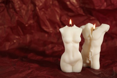 Beautiful burning male and female body shaped candles on red crumpled parchment. Space for text