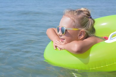 Little girl with inflatable ring in sea on sunny day, space for text