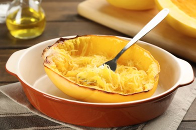 Photo of Half of cooked spaghetti squash and fork in baking dish on table, closeup