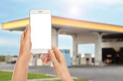 Woman paying for refueling via smartphone at gas station, closeup. Device with empty screen